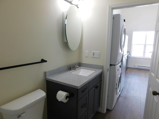 bathroom featuring vanity, wood finished floors, stacked washer and dryer, a baseboard heating unit, and toilet