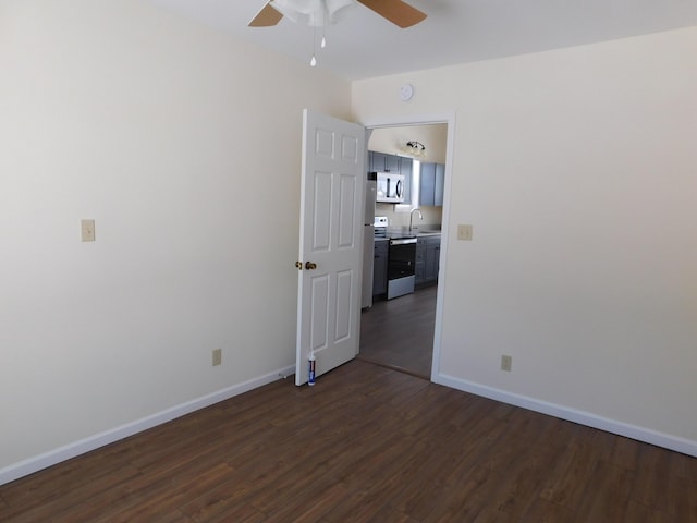 unfurnished room featuring a sink, baseboards, ceiling fan, and dark wood-style flooring