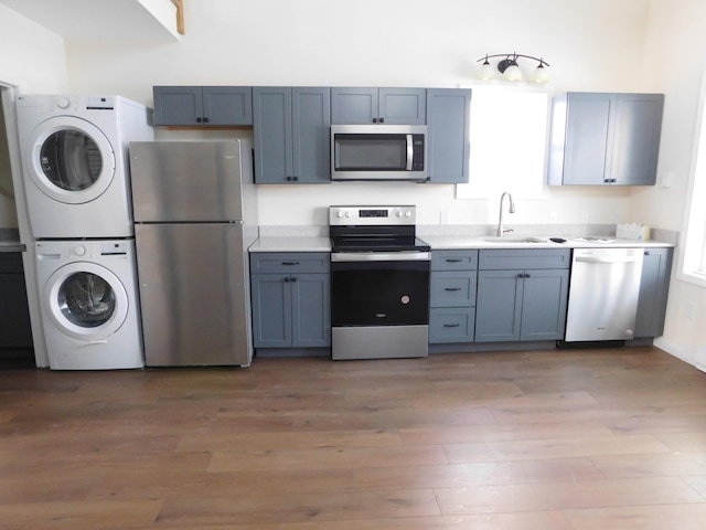 kitchen featuring stacked washer / dryer, light countertops, light wood-style flooring, appliances with stainless steel finishes, and a sink