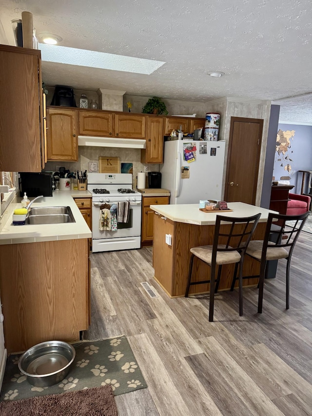 kitchen featuring a breakfast bar, light countertops, light wood-style flooring, white appliances, and a sink