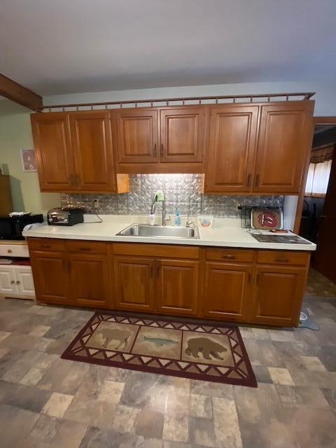 kitchen featuring light countertops, brown cabinets, tasteful backsplash, and a sink