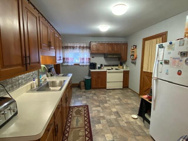 kitchen featuring stone finish flooring, under cabinet range hood, light countertops, white appliances, and a sink