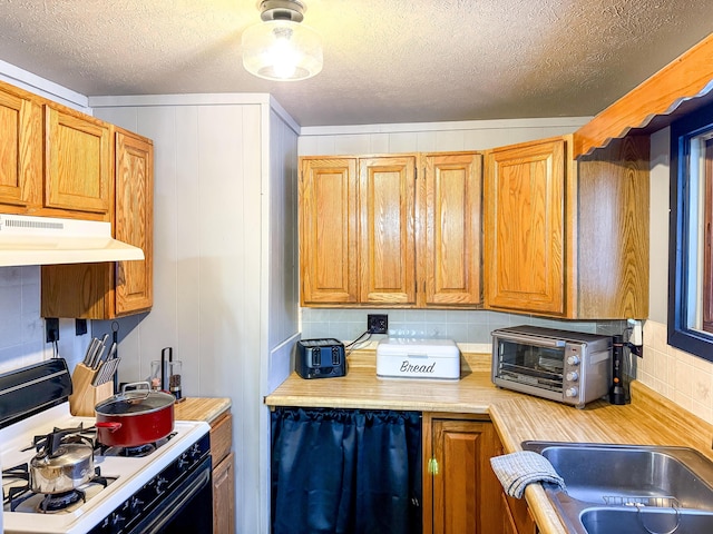 kitchen with gas range, light countertops, tasteful backsplash, and under cabinet range hood