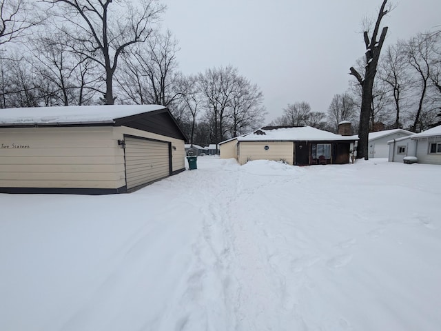 snowy yard featuring an outbuilding and a detached garage