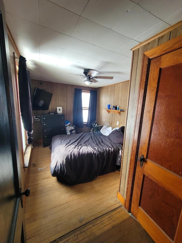 bedroom with wooden walls, wood-type flooring, and ceiling fan