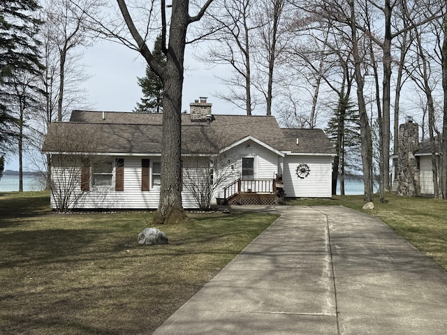 view of front facade with a front lawn, roof with shingles, a chimney, concrete driveway, and a water view
