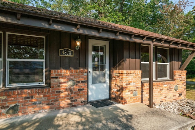 doorway to property featuring brick siding, covered porch, and board and batten siding