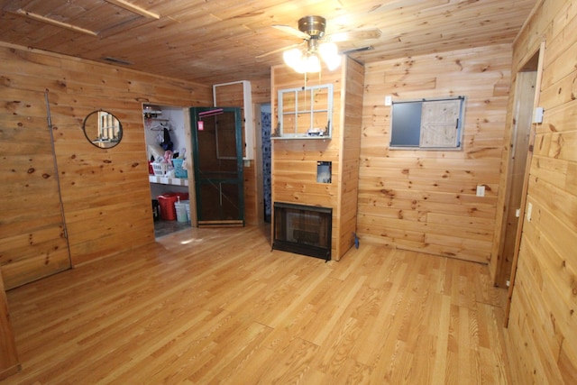 spare room with wooden walls, wood ceiling, light wood-type flooring, and a ceiling fan