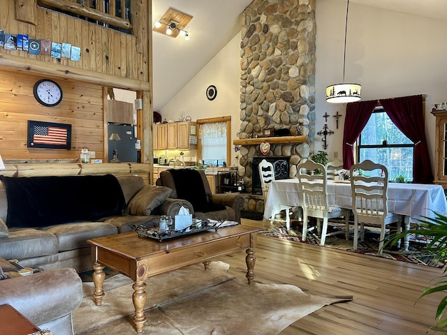 living room featuring high vaulted ceiling, a stone fireplace, and wood finished floors