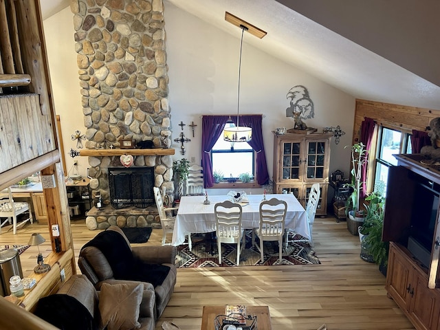 dining space with light wood-type flooring, high vaulted ceiling, a healthy amount of sunlight, and a fireplace