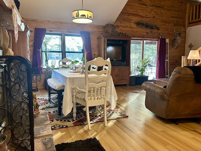 dining area featuring light wood finished floors, wood walls, and high vaulted ceiling