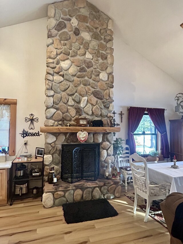 living area featuring a stone fireplace, light wood-style flooring, and high vaulted ceiling