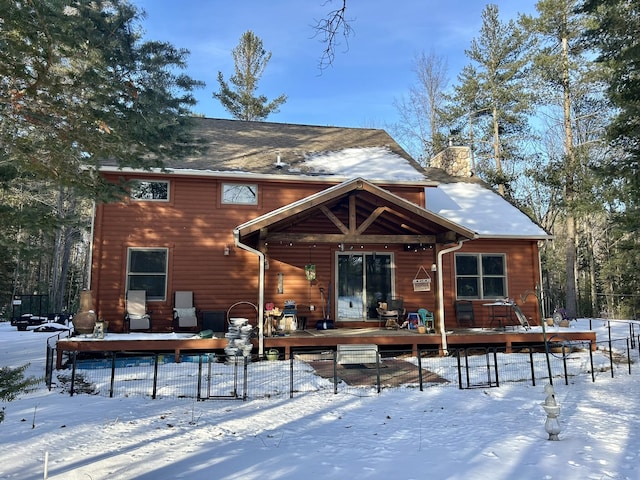 snow covered house with a deck, fence, and a chimney