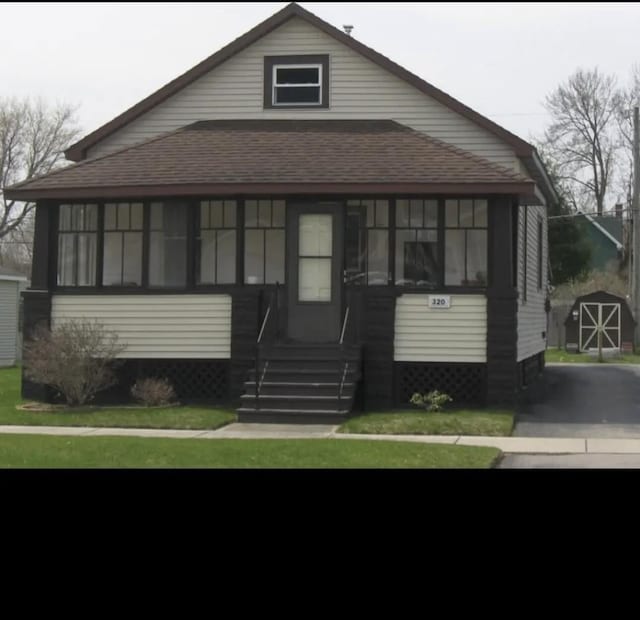 view of front of house with an outbuilding, entry steps, a front yard, and a sunroom