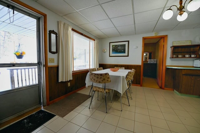 dining room featuring a wainscoted wall, wood walls, light tile patterned floors, a notable chandelier, and a paneled ceiling