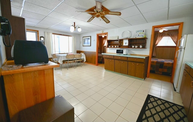 kitchen with a wainscoted wall, a paneled ceiling, brown cabinets, and freestanding refrigerator