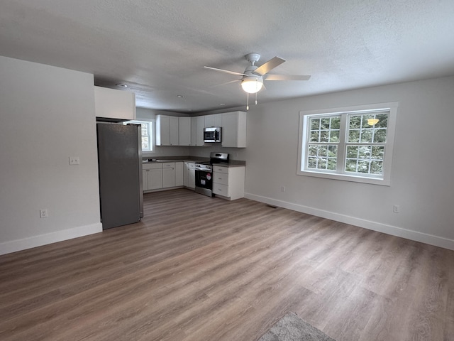 kitchen with a healthy amount of sunlight, baseboards, light wood-style flooring, stainless steel appliances, and dark countertops