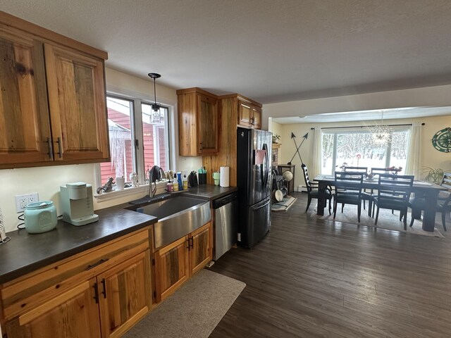 kitchen with dark countertops, stainless steel dishwasher, freestanding refrigerator, brown cabinetry, and a sink