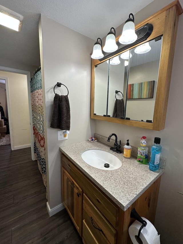 full bath featuring a textured ceiling, vanity, baseboards, and wood finished floors