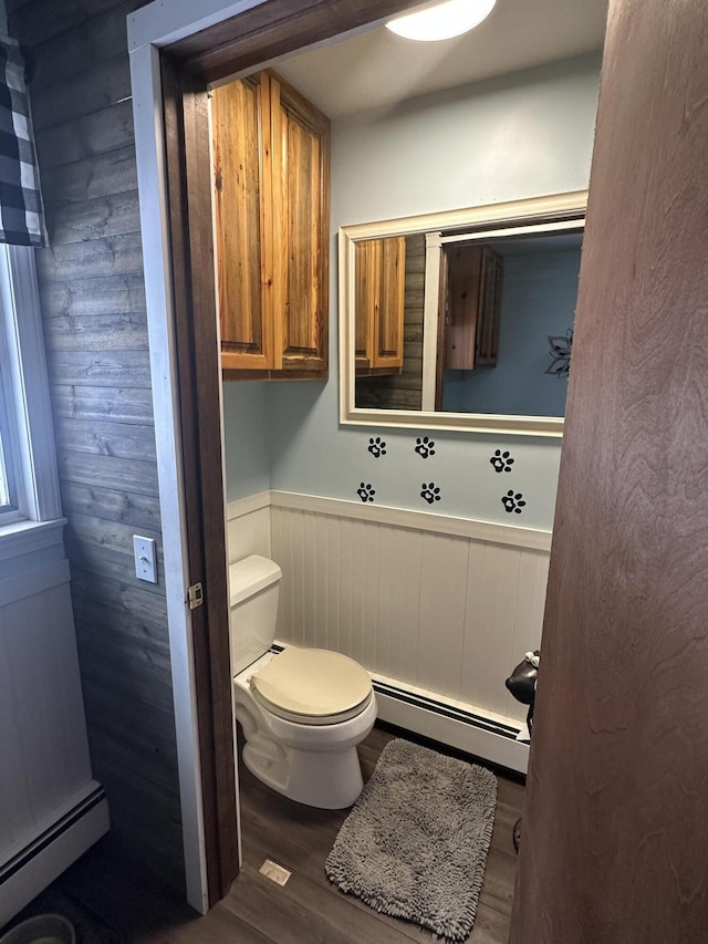 bathroom featuring toilet, wood finished floors, baseboard heating, and wainscoting