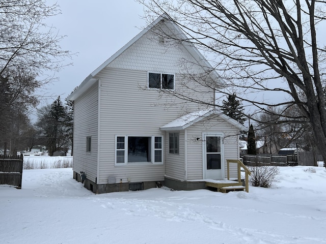 snow covered rear of property featuring a garage and fence