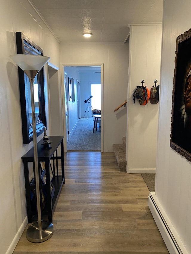 corridor with stairway, ornamental molding, a baseboard heating unit, and wood finished floors