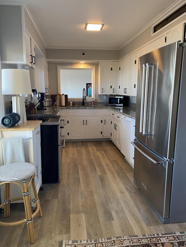 kitchen with white cabinets, ornamental molding, wood finished floors, and stainless steel appliances