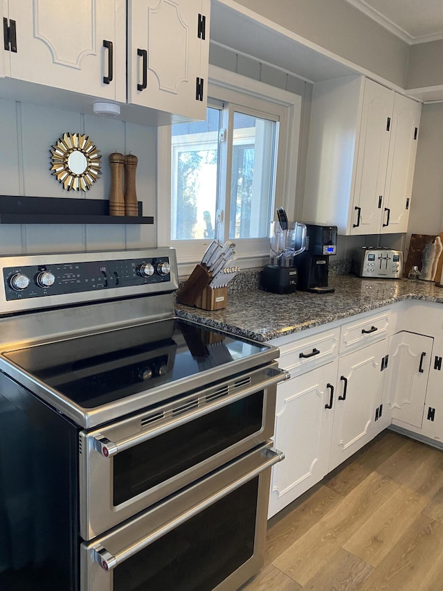 kitchen featuring stone counters, range with two ovens, ornamental molding, white cabinets, and light wood-style floors