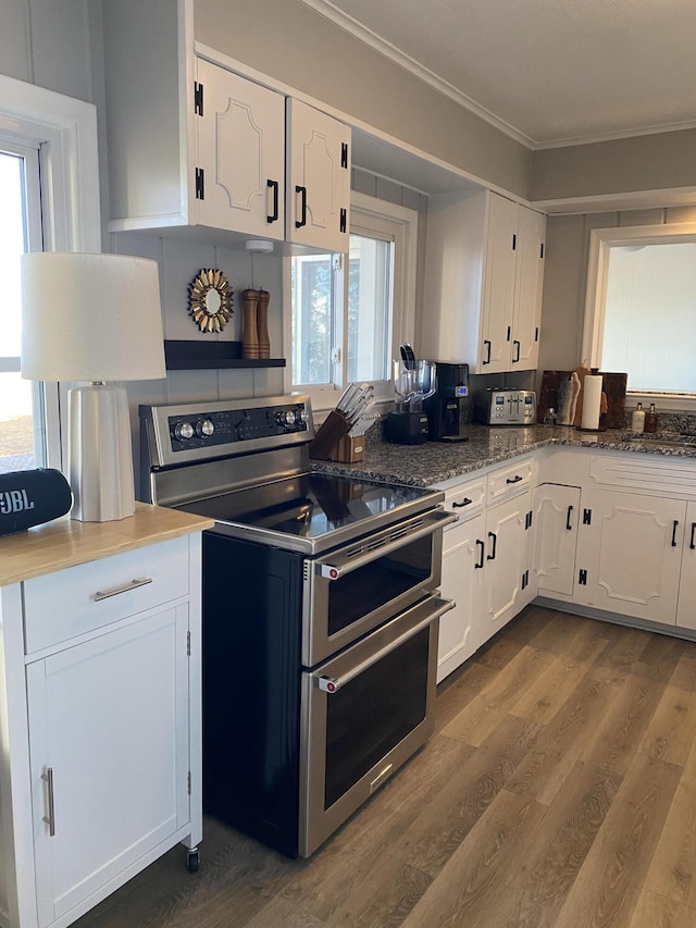 kitchen with dark wood-style floors, double oven range, dark stone counters, ornamental molding, and white cabinets