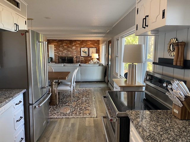 kitchen with dark stone countertops, appliances with stainless steel finishes, white cabinets, brick wall, and light wood finished floors