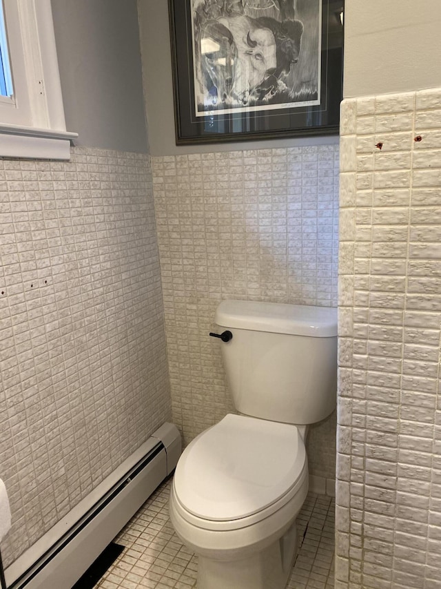 bathroom with a wainscoted wall, baseboard heating, tile walls, toilet, and tile patterned floors