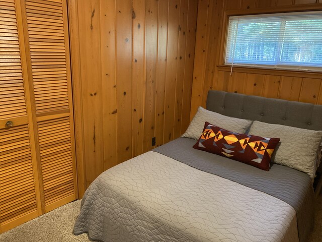 carpeted bedroom with a closet and wooden walls