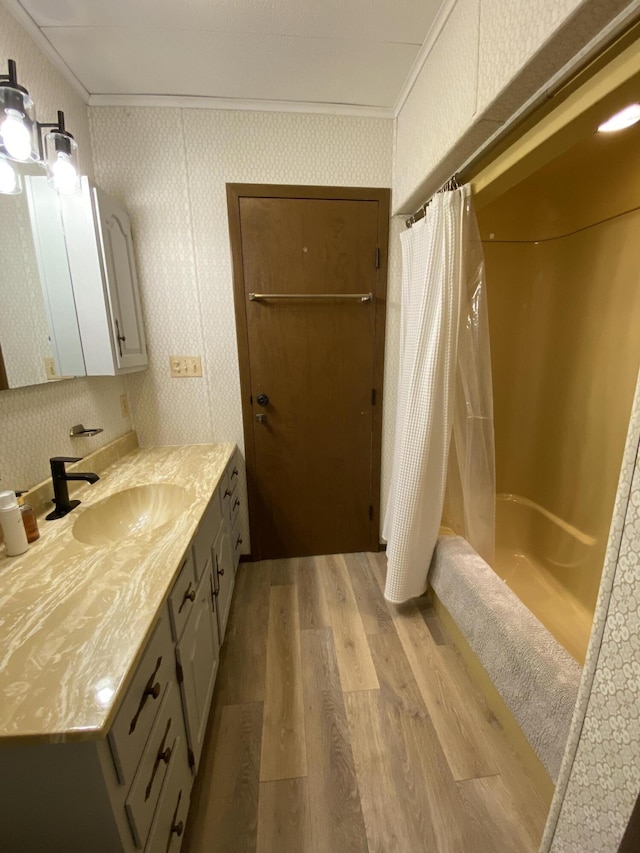 bathroom with wallpapered walls, crown molding, wood finished floors, shower / bath combination with curtain, and vanity