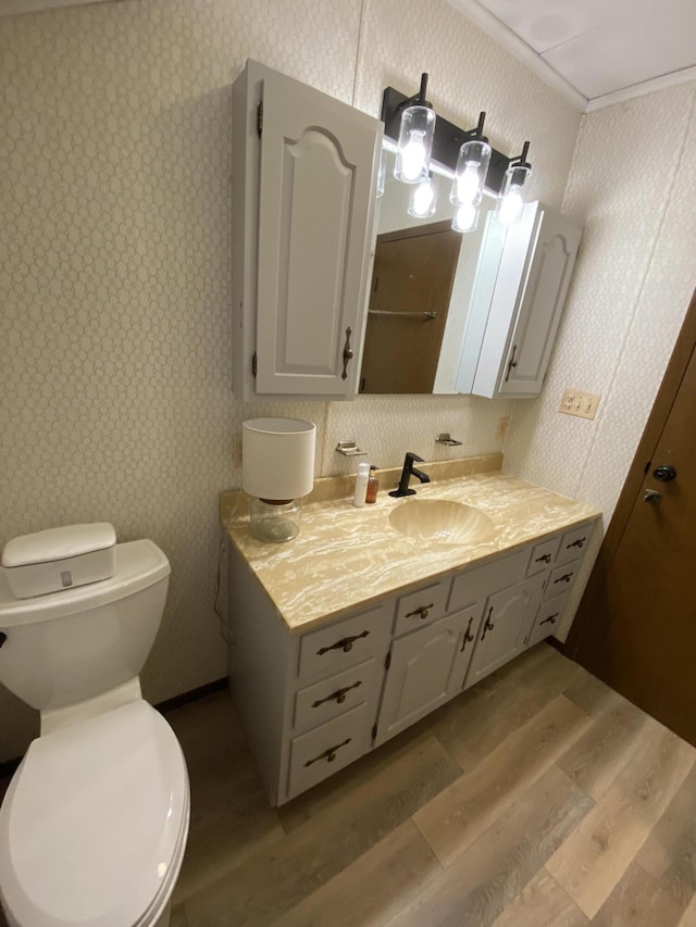 bathroom with toilet, wood finished floors, crown molding, and wallpapered walls