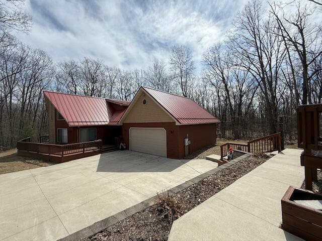 view of property exterior with an attached garage, a wooden deck, metal roof, and driveway