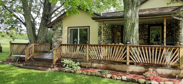 back of property with stone siding, stucco siding, a wooden deck, and roof with shingles