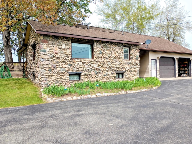 8110 Perry Rd, Houghton Lake, MI 48629 - view of front of house featuring stone siding, asphalt driveway, an attached garage, and roof with shingles