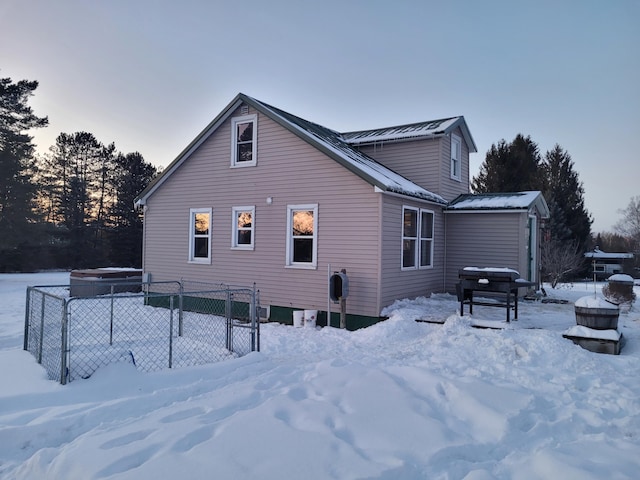 snow covered rear of property with a gate, fence, and metal roof