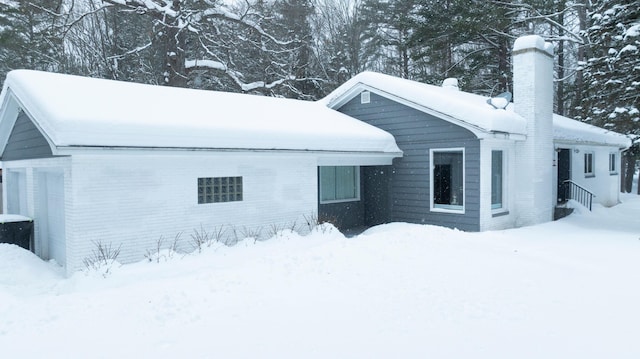 view of snowy exterior with brick siding and a chimney