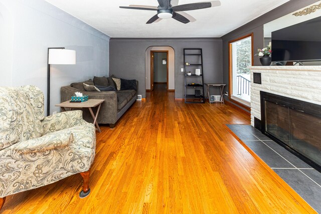 208 Stuckey Ave, Roscommon, MI 48653 - living area featuring a ceiling fan, a fireplace with flush hearth, wood finished floors, baseboards, and arched walkways
