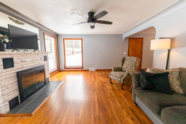 208 Stuckey Ave, Roscommon, MI 48653 - living area featuring a textured ceiling, visible vents, hardwood / wood-style flooring, a ceiling fan, and a stone fireplace