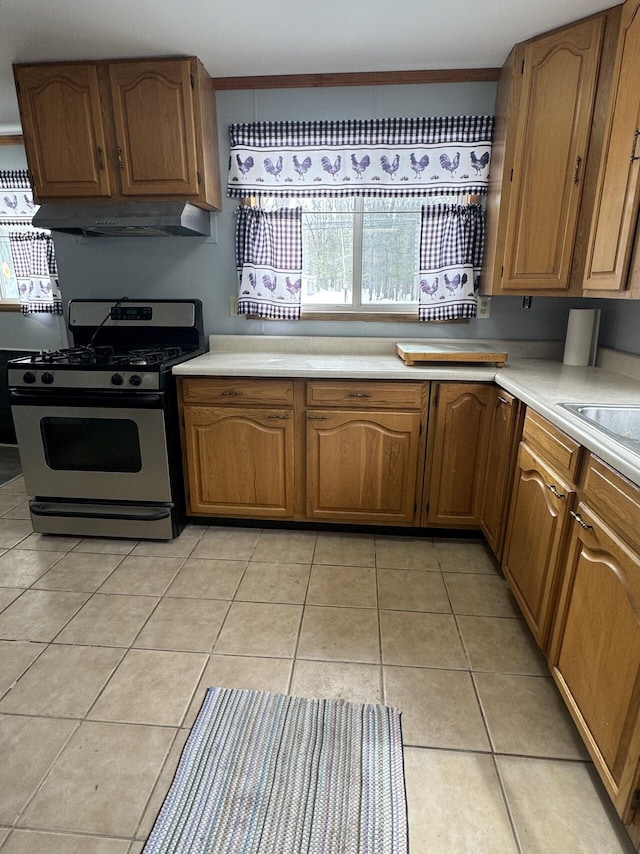 kitchen featuring light tile patterned floors, brown cabinetry, stainless steel gas range, light countertops, and under cabinet range hood