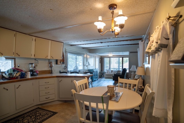 kitchen featuring open floor plan, beam ceiling, an inviting chandelier, a textured ceiling, and white cabinetry