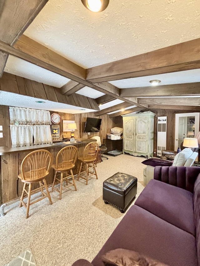 living area featuring wooden walls, a bar, a textured ceiling, beamed ceiling, and light colored carpet