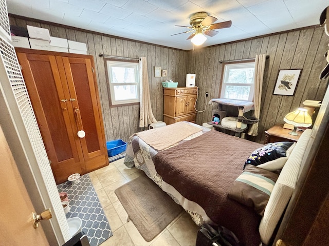 bedroom featuring light tile patterned flooring, wooden walls, crown molding, and a ceiling fan