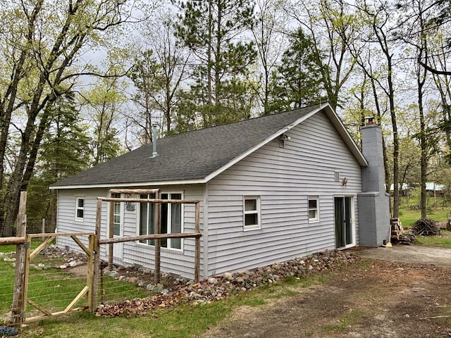 4804 Basil Dr, Comins, MI 48619 - view of side of home featuring a shingled roof, a chimney, and fence