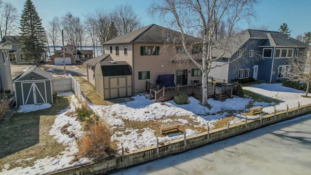 snow covered back of property with fence, a residential view, a wooden deck, a storage shed, and an outdoor structure