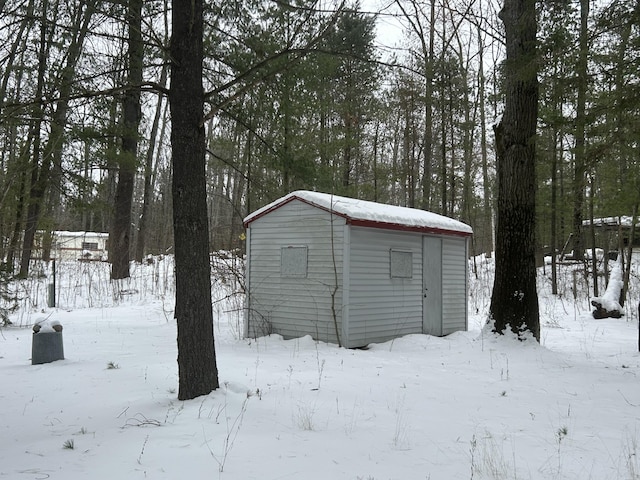 snow covered structure featuring a storage shed and an outbuilding