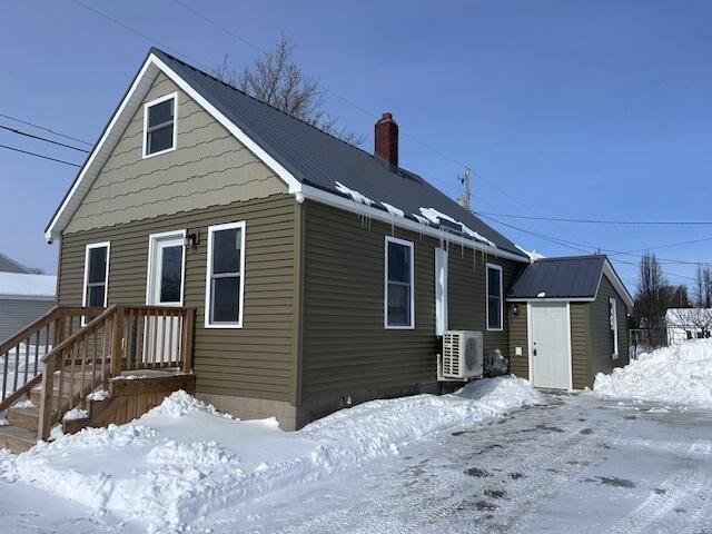 snow covered back of property featuring ac unit, a storage unit, an outdoor structure, and a chimney