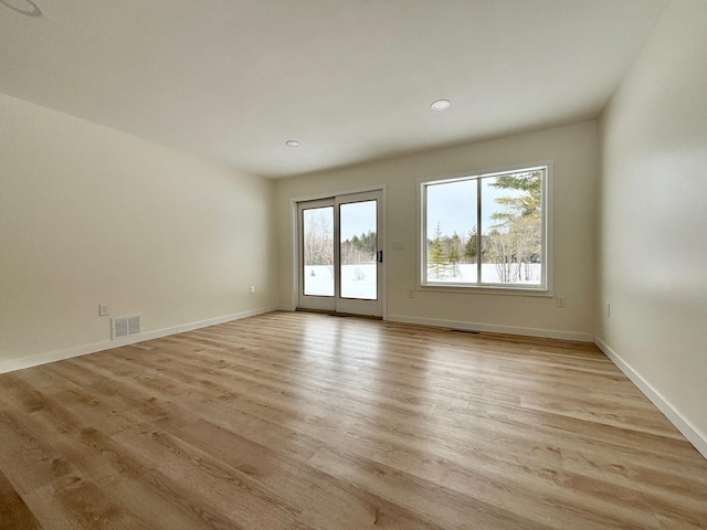 empty room with visible vents, light wood-type flooring, and baseboards